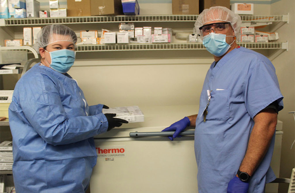 Margaret Brown, PharmD, and Christopher Coccari, RN place the COVID vaccine in the freezer.