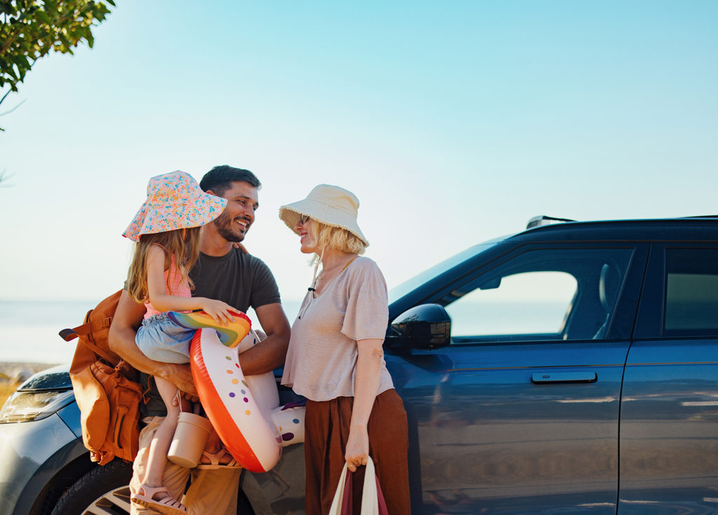 Family with sun hats standing by a car near the beach, holding summer items, illustrating sun safety and outdoor skin protection.